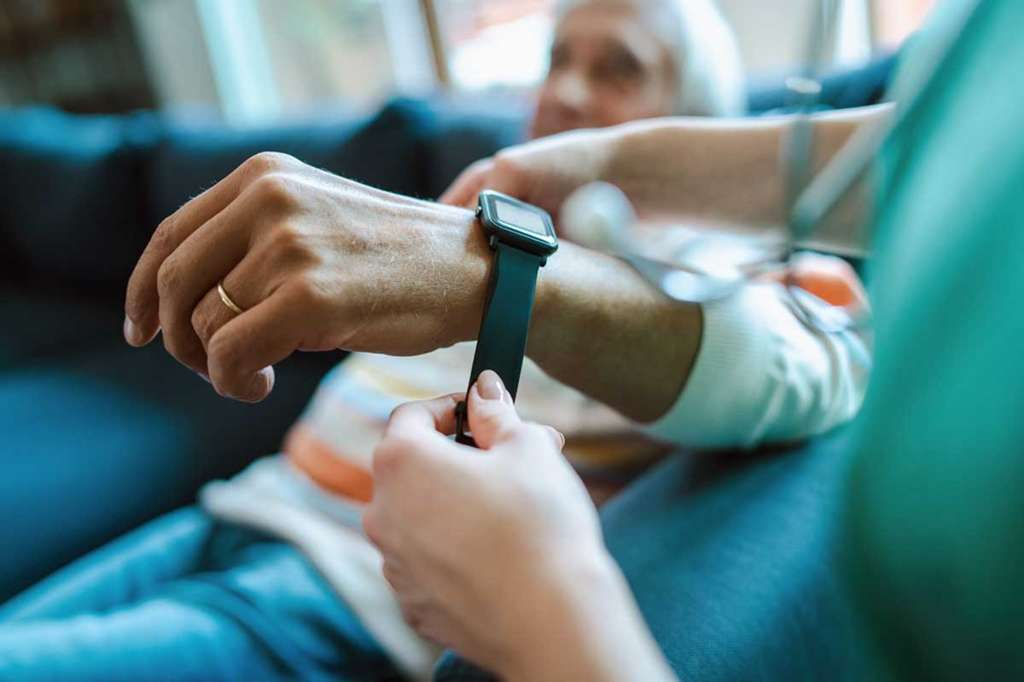 A caregiver adjusts a smart medical watch on an elderly person's wrist, a key tool for remote health monitoring
